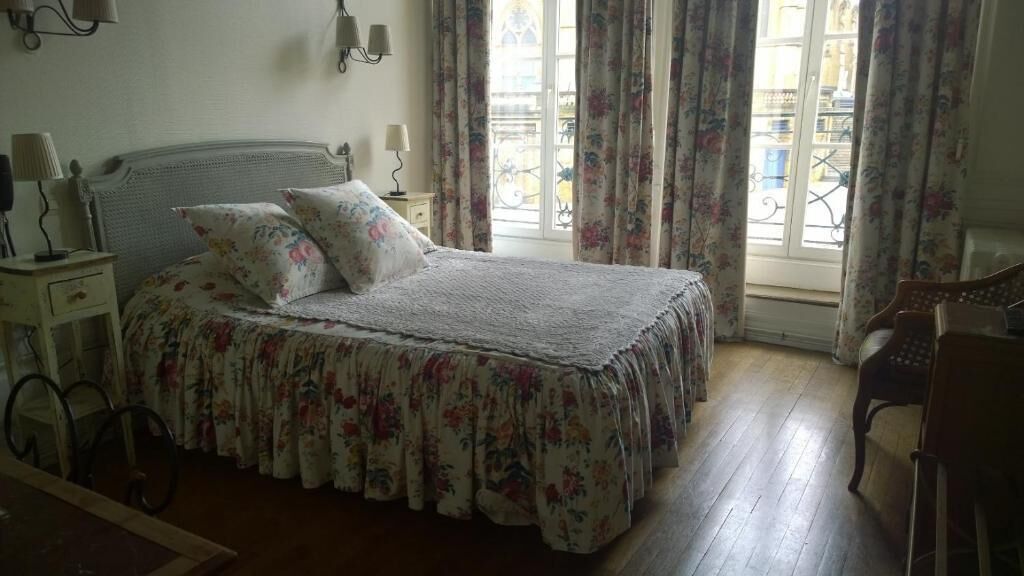Een slaapkamer met een bed, bloemen gordijnen, een raam met uitzicht en een houten vloer.