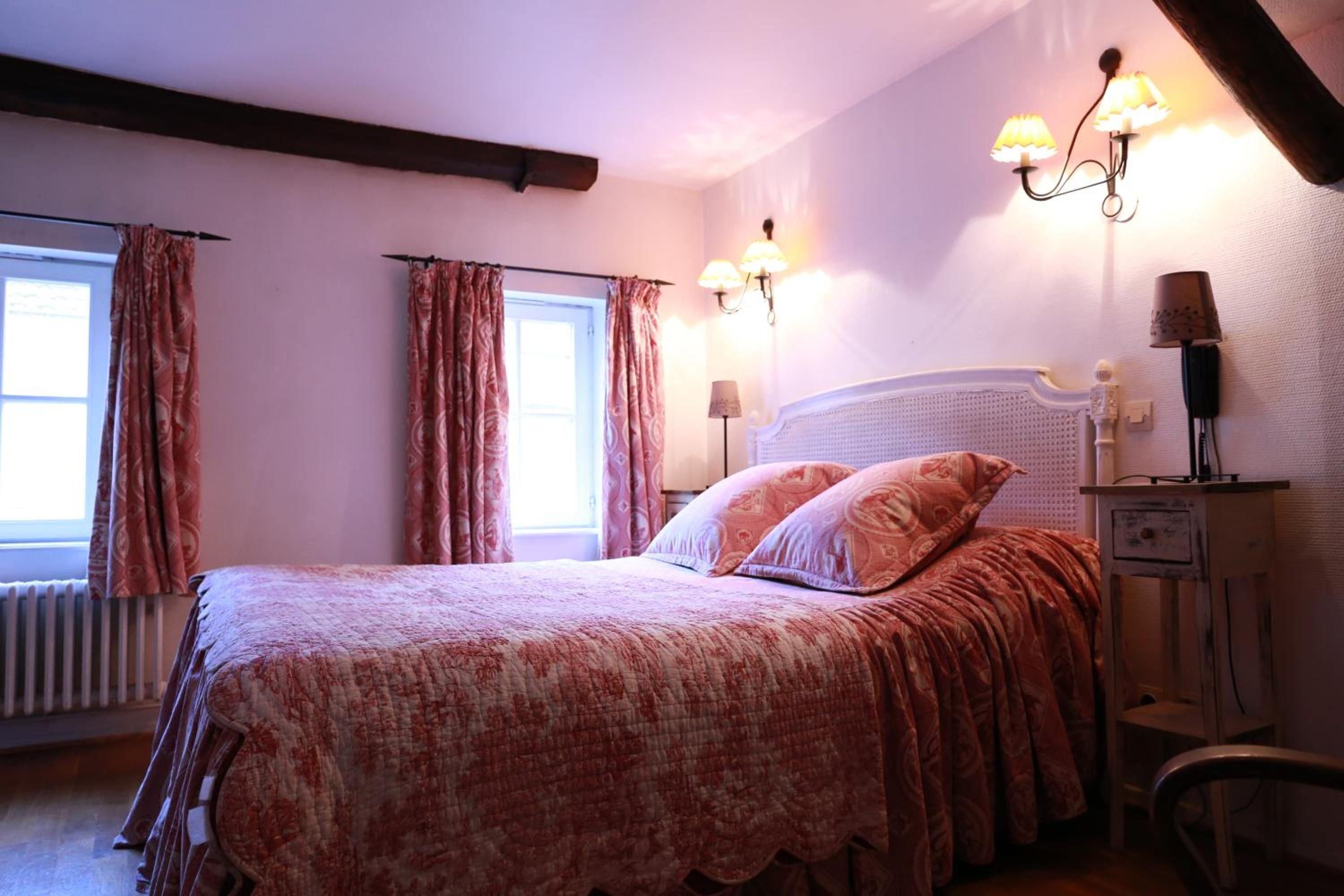Une chambre à coucher avec un grand lit, deux lampes de chevet, une table de chevet et une fenêtre avec des rideaux.