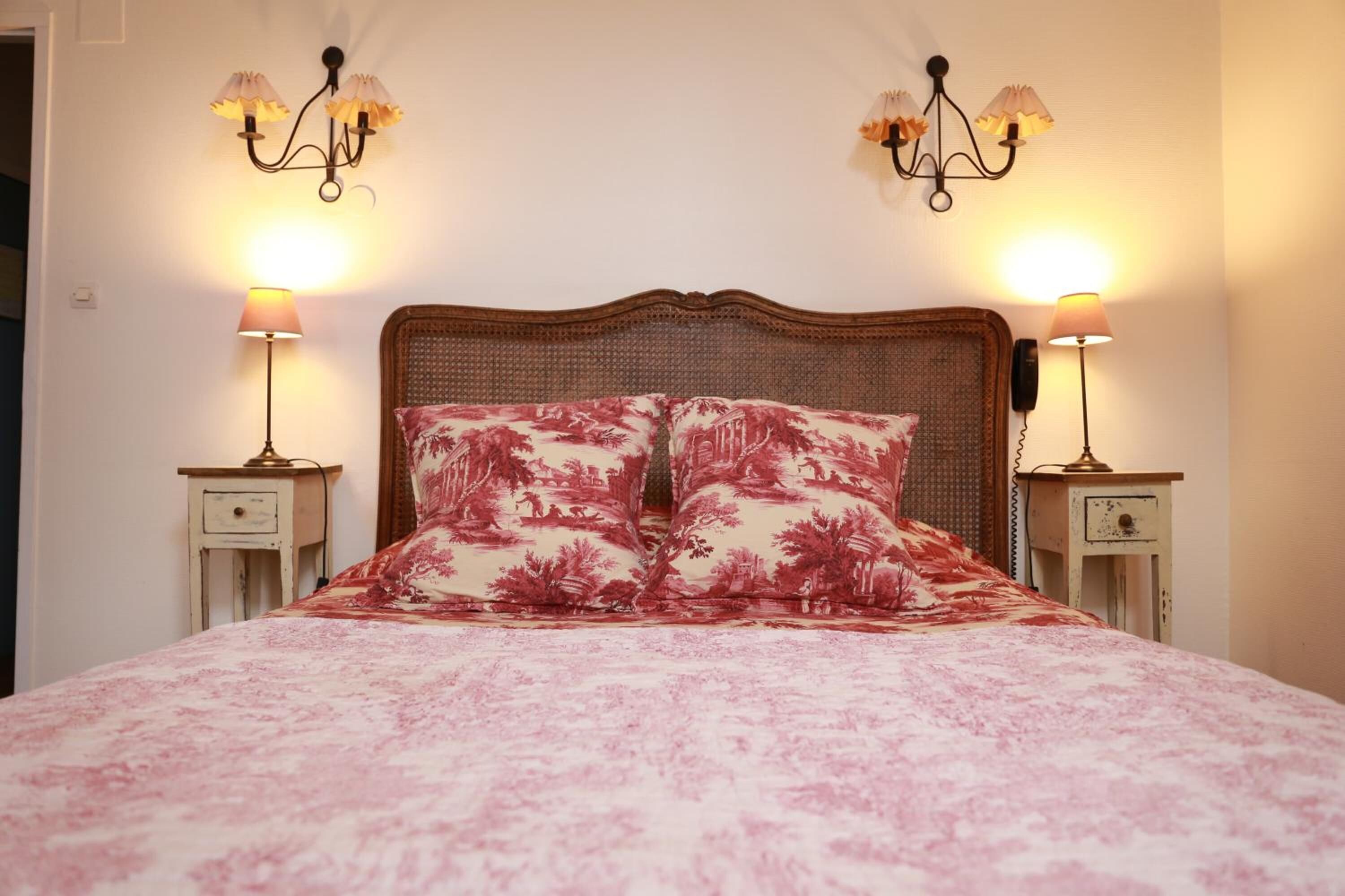 A bed with a floral bedspread and two matching pillows, flanked by two bedside tables with lamps and a telephone.
