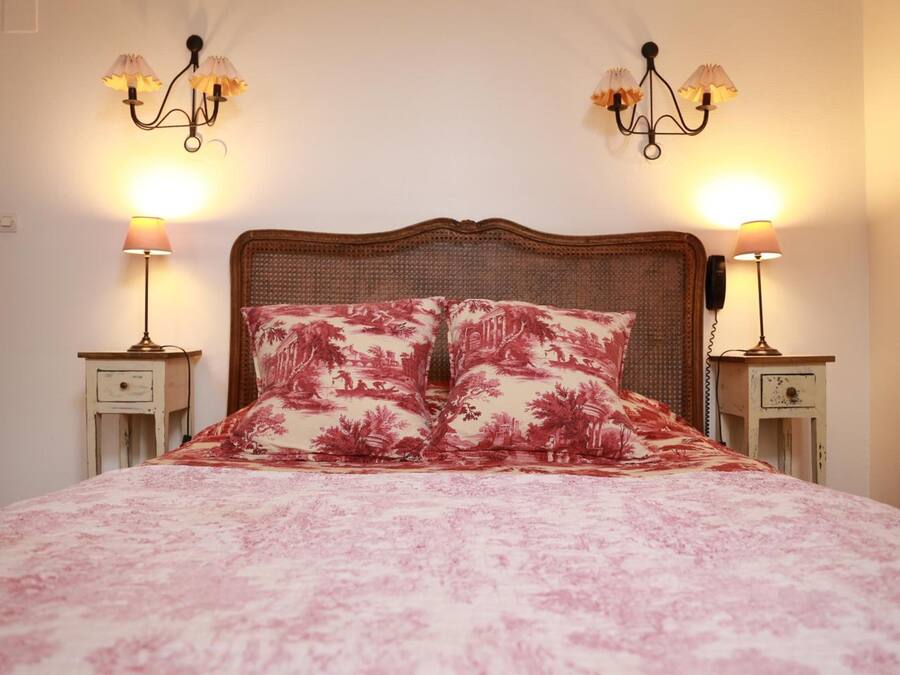 A bed with a floral bedspread and two matching pillows, flanked by two bedside tables with lamps and a telephone.