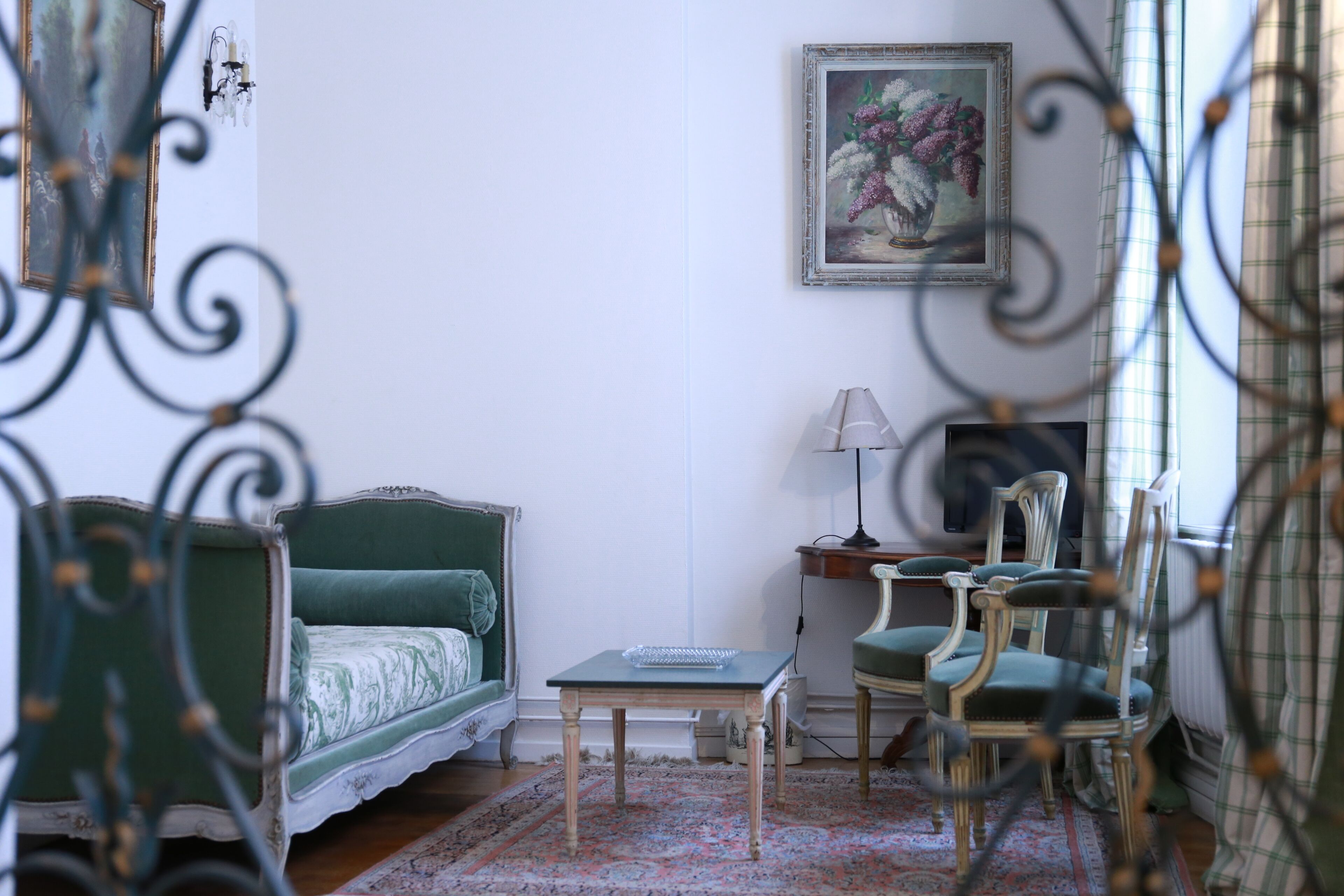 Una habitación con un sofá verde, una mesita, una silla y un cuadro en la pared.