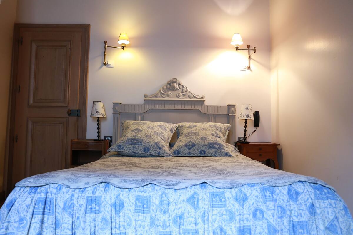 A bedroom with a large bed, two bedside lamps, a wooden door, and a nightstand with a lamp.