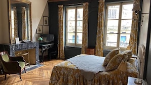 Quarto com cama, escrivaninha, cadeira e uma grande janela com cortinas.
