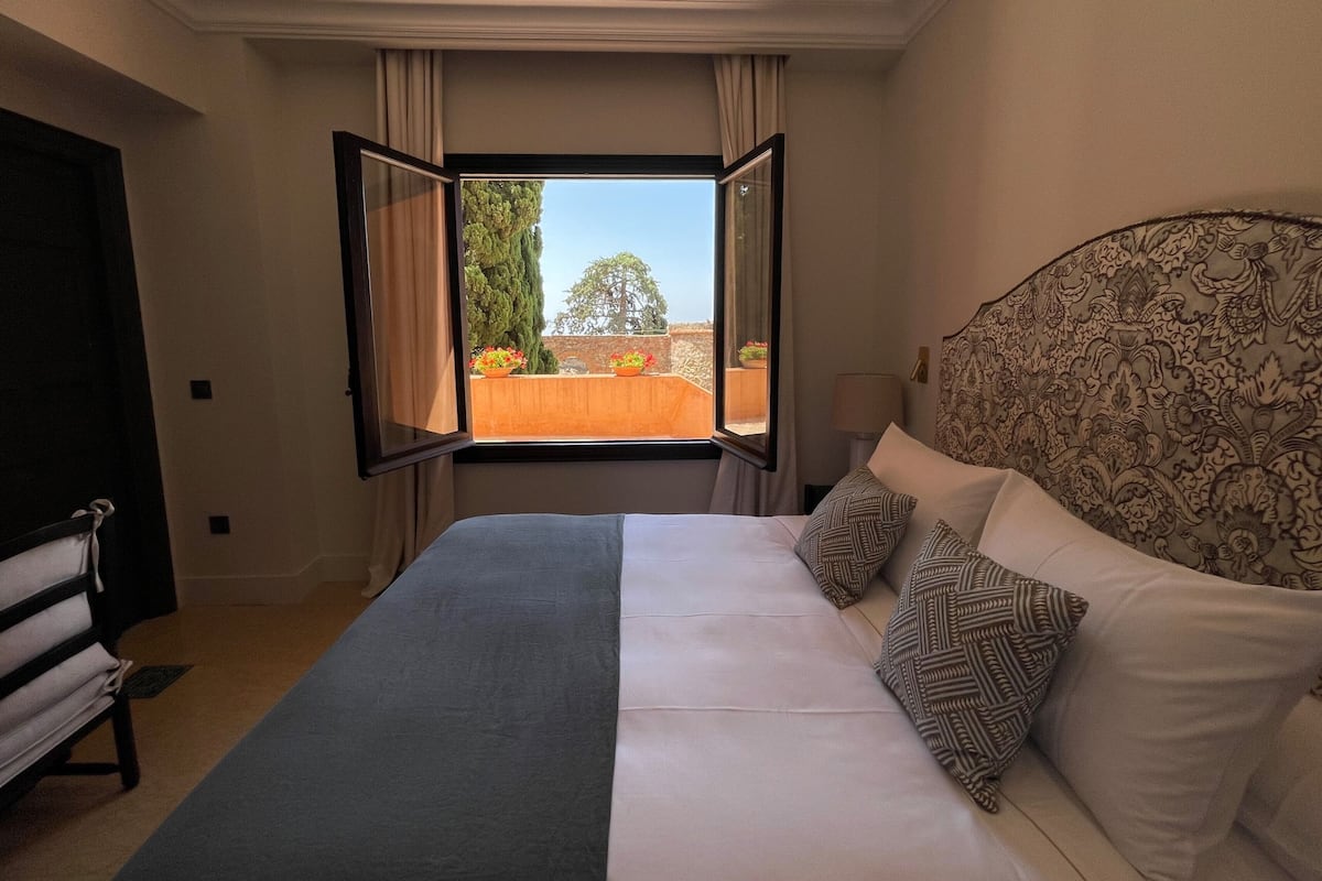 A hotel room with a bed, a window with curtains, a headboard, and a nightstand.
