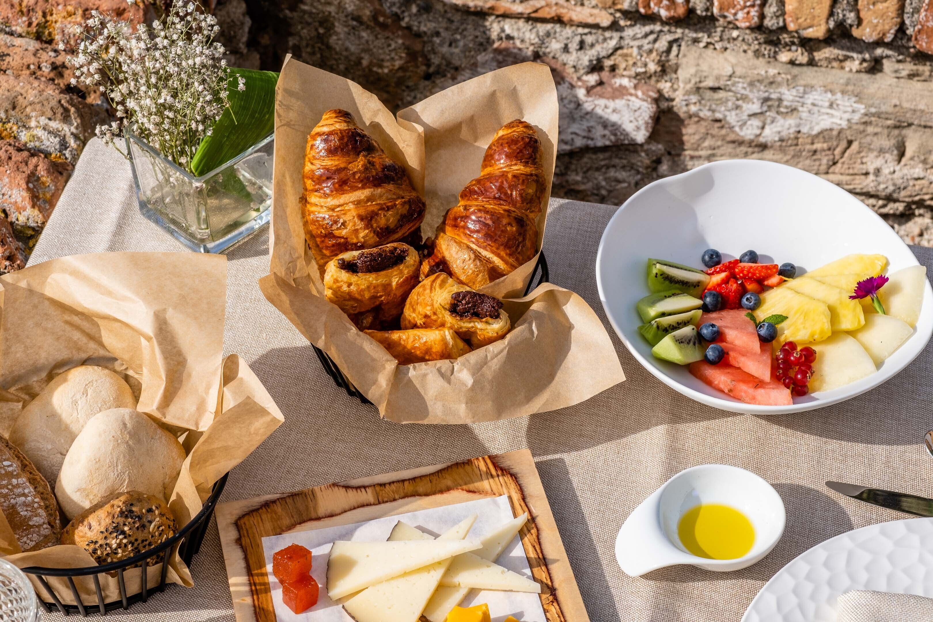 A breakfast setting with pastries, bread, cheese, and a fruit bowl.