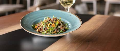 A plate of food on a wooden table with a glass of white wine.
