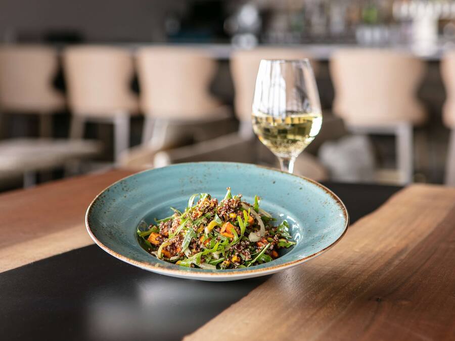 A plate of food on a wooden table with a glass of white wine.