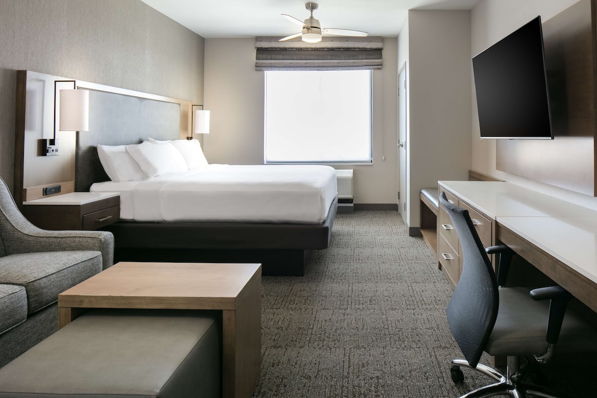A hotel room with a bed, a desk, a chair, a television, and a window.
