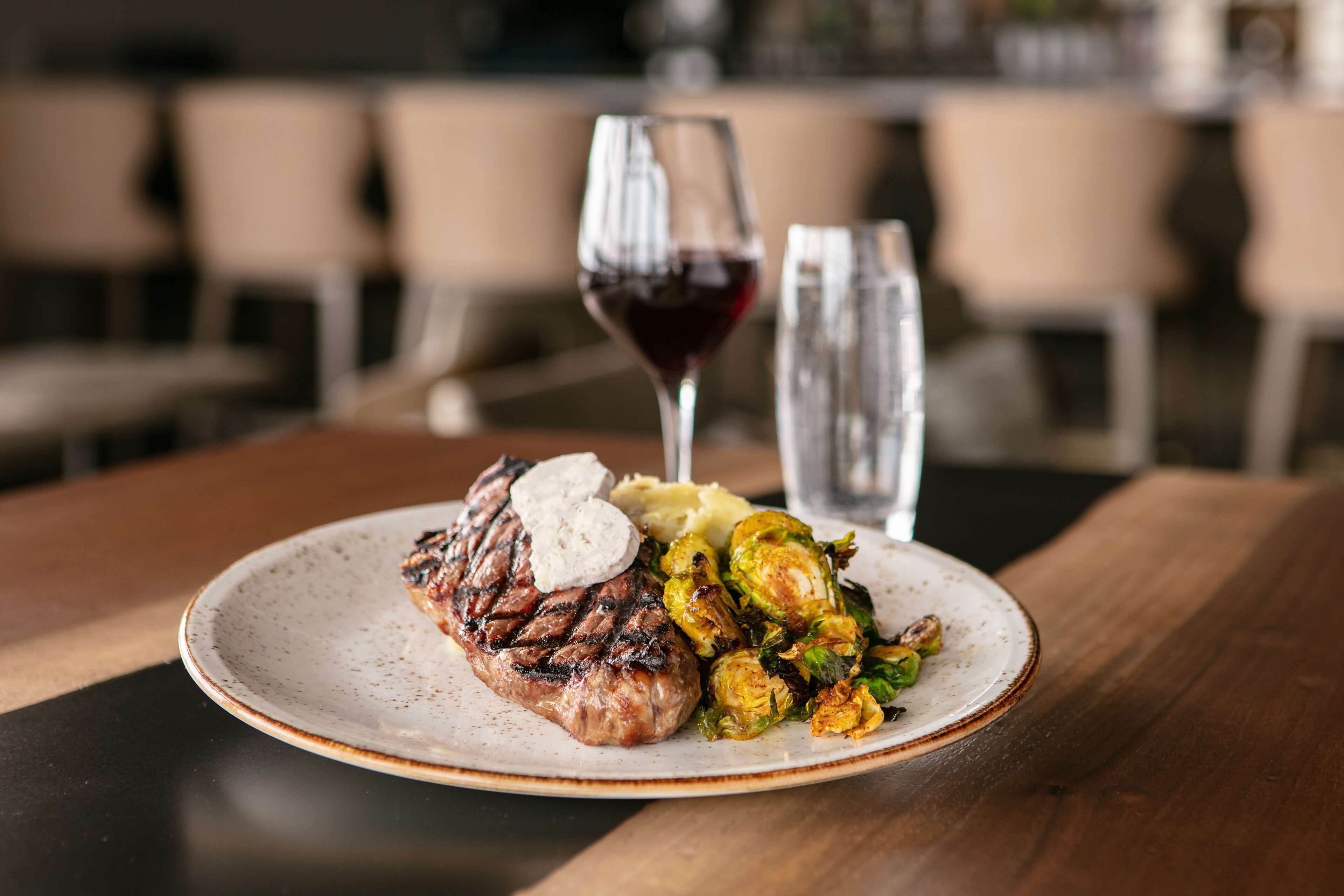 Um prato com bife, purê de batatas e brócolis de Bruxelas em cima de uma mesa de madeira.