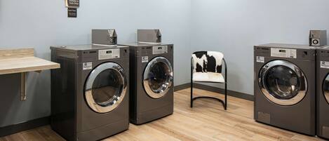 A laundry facility with four front-loading washing machines, a wooden bench, and a chair.
