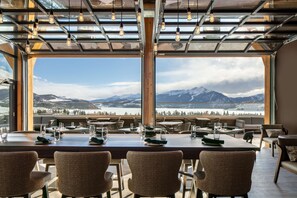 A dining area with a table set for six, large windows offering a mountain view, and a modern ceiling design with exposed beams and hanging lights. - Homewood Suites by Hilton Dillon (Dillon)