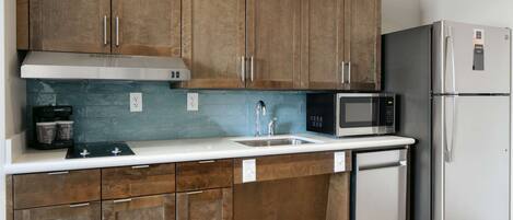 A modern kitchen with wooden cabinets, a stainless steel refrigerator, a microwave, and a dishwasher.