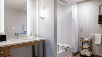 Un baño moderno con lavamanos, espejo, ducha y toallero con toallas.