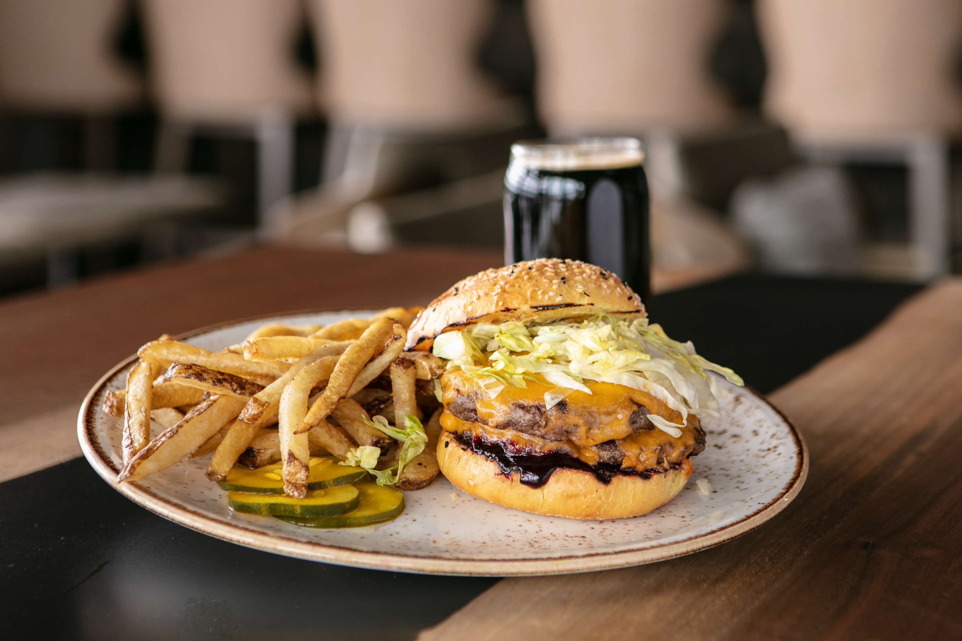 A plate with a burger, fries, and pickles on a table.