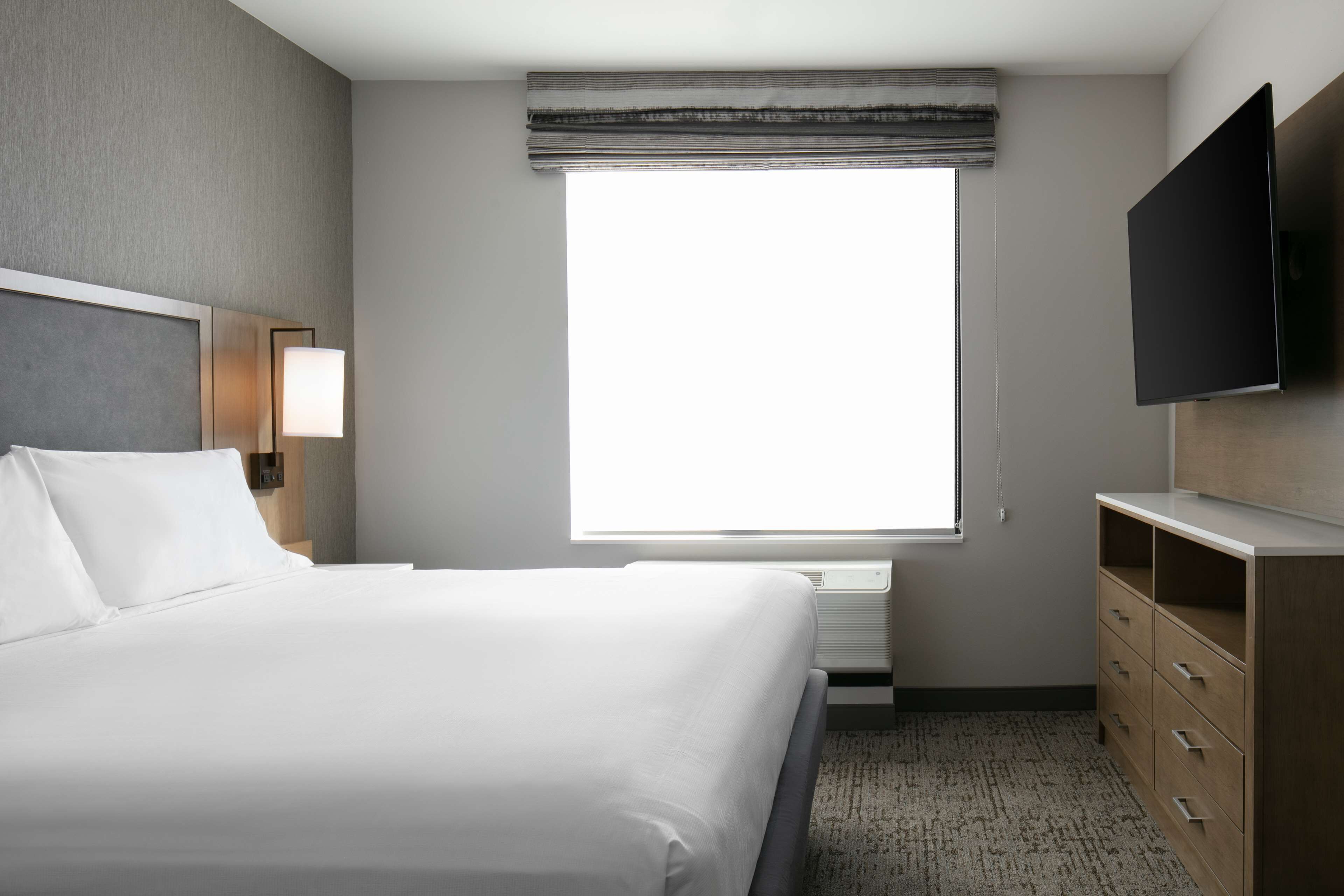 Une chambre d’hôtel avec un grand lit, un téléviseur à écran plat, une lampe de chevet et une fenêtre donnant sur un beau paysage.