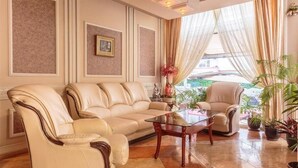A living room with a beige sofa, a matching armchair, and a glass coffee table. There are potted plants and a picture frame on the wall. - Imperial Hotel (Primorsko)