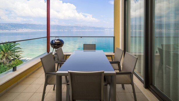 Ein Balkon mit Tisch und Stühlen, mit Blick auf ein Gewässer und das entfernte Land.