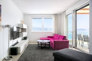 Ein modernes Wohnzimmer mit einer Couch, einem Couchtisch, einem Flachbildfernseher und einer Glastür, die auf einen Balkon führt.
