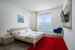 Ein modernes Schlafzimmer mit Bett, Nachttischen, einem roten Teppich, einem blauen Sessel, einem Gemälde und einem an der Wand befestigten Fernseher.