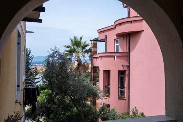 A pink building with balconies, a view of the sea, and a palm tree.