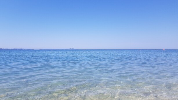 A clear view of a beach with shallow water revealing rocks and pebbles.