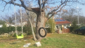A tree with a tire swing hanging from its branches, a green swing, and a house with a solar panel roof in the background.