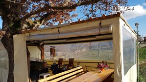 A wooden bench and table under a covered area with a view of trees and hills.