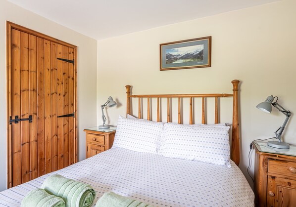 Une chambre à coucher avec un lit en bois, deux tables de chevet avec des lampes, une armoire en bois et un tableau encadré au mur.