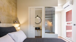 A bedroom with a bed, pillows, a bedside table, a mirror, a door leading to a bathroom, and an air conditioning unit. - Palermo Magic House (palermo)