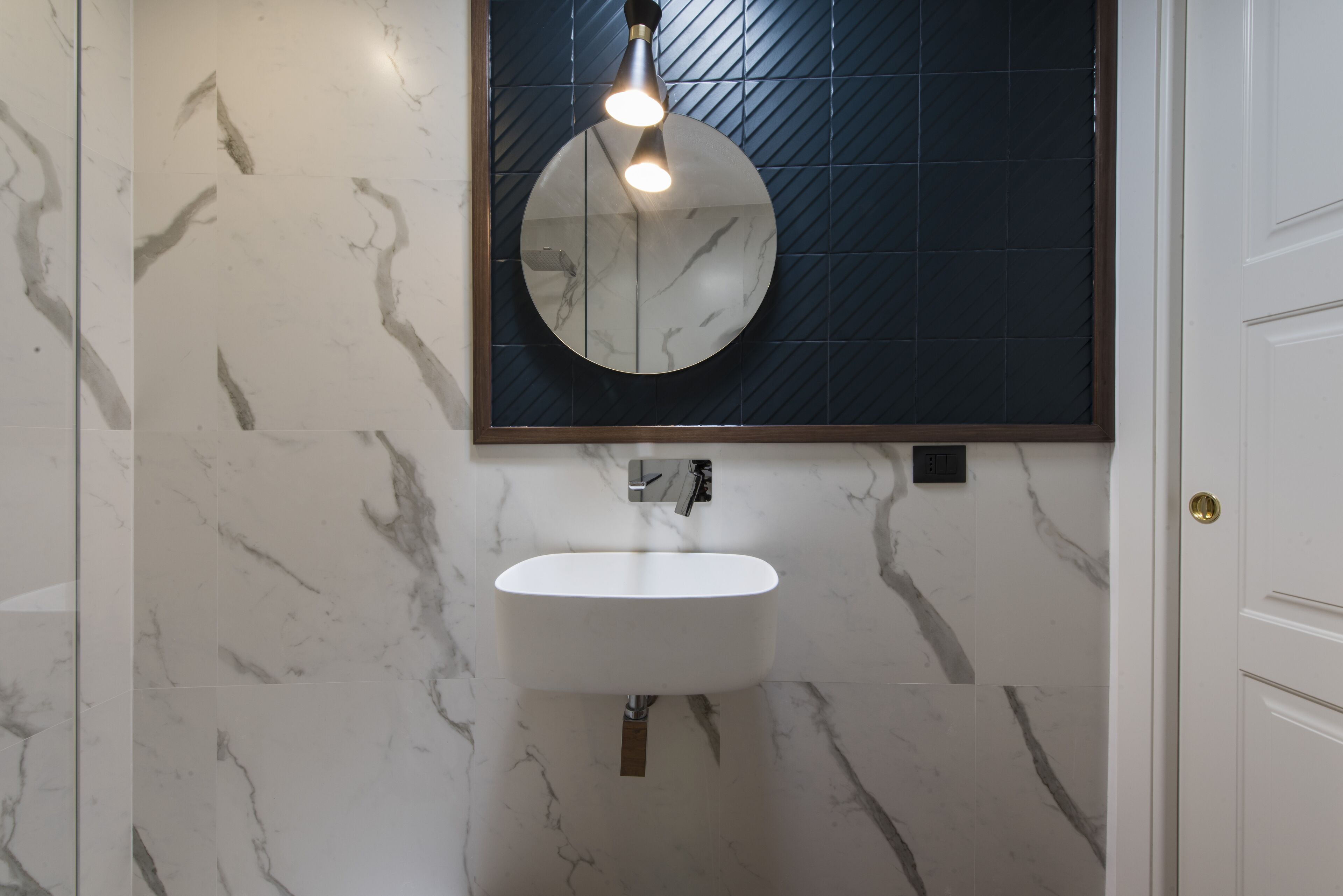 A bathroom with a white sink, a round mirror, and a light fixture above the mirror.