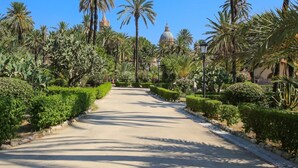 A paved pathway flanked by neatly trimmed hedges and palm trees, leading towards a building with a dome. - Palermo Magic House (palermo)