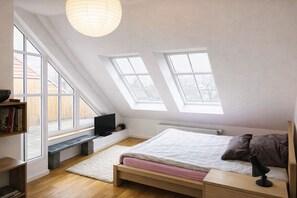 A bedroom with a sloped ceiling, skylights, a bed, a bedside table, a TV, and a bookshelf. - Mauerpark Mitte-Prenzl.Berg Penthouse, modern and authentic. 3 BR, 2 Bath (Berlin)