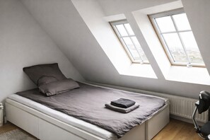 A small, sloped bedroom with a bed, two windows, and a radiator.