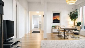 Ein modernes Wohnzimmer mit Flachbildfernseher, einer Essecke mit Tisch und Stühlen, einer großen Pflanze und einem Poster an der Wand.