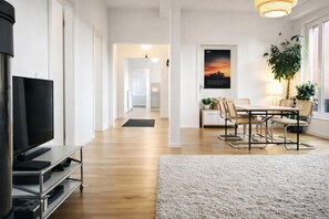 A modern living room with a flat-screen TV, a dining area with a table and chairs, a large plant, and a poster on the wall. - Mauerpark Mitte-Prenzl.Berg Penthouse, modern and authentic. 3 BR, 2 Bath (Berlin)