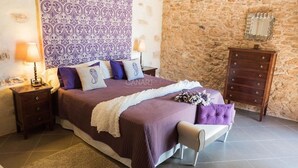 A bedroom with a large bed, a wooden dresser, a stone wall, and patterned wallpaper. - Casa Rural La Morisca (Tuineje)