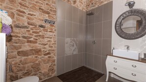 A bathroom with a stone wall, a shower, a sink, and a mirror. - Casa Rural La Morisca (Tuineje)