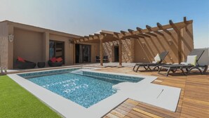 A modern outdoor pool area with a pergola, lounge chairs, and a small seating area with cushions. - Casa Rural La Morisca (Tuineje)