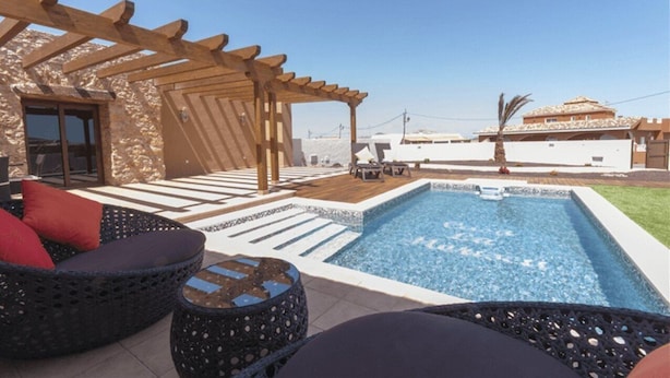 A pool area with a pergola, wicker furniture, and a view of a building in the background. - Casa Rural La Morisca (Tuineje)