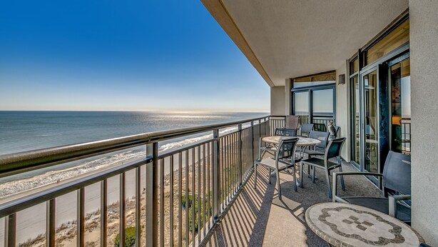 Ein Balkon mit Blick auf Strand und Meer, ausgestattet mit Stühlen und einem Tisch.