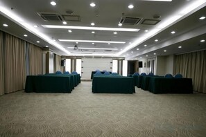 Une salle de conférence dotée de plusieurs tables et chaises, d’un sol recouvert de moquette et d’un plafond haut avec des luminaires encastrés.