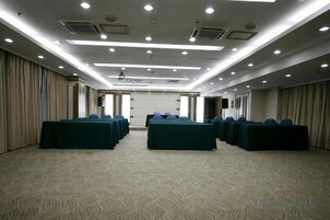Un salón de conferencias con varias mesas y sillas, suelo alfombrado y un techo alto con iluminación empotrada.