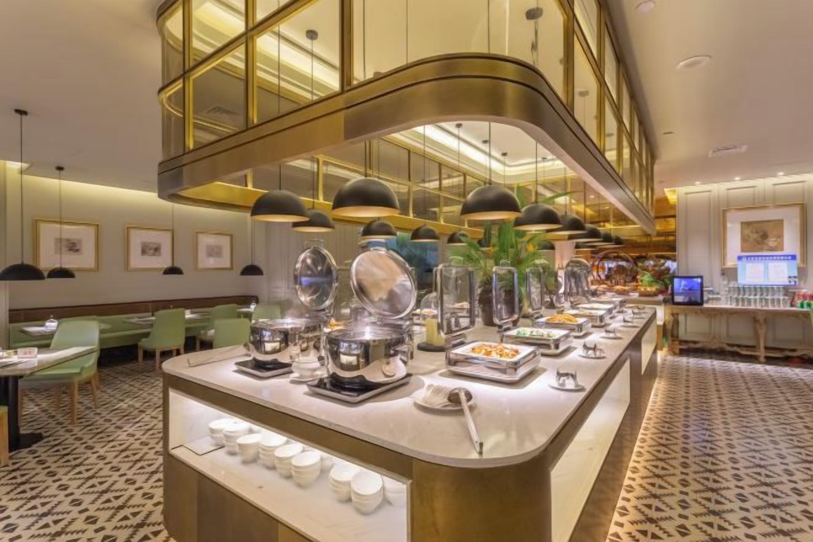 Zona de desayuno de hotel con barra de buffet, que incluye diversos alimentos y una estación de café.