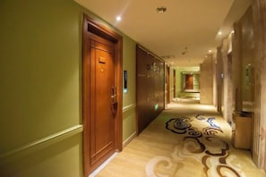 A hotel corridor with a wooden door, a patterned carpet, and a hallway leading to a room.