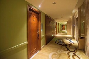 Un pasillo de hotel con una puerta de madera, una alfombra estampada y un pasillo que conduce a una habitación.