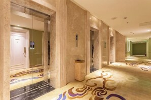Un couloir d’hôtel aux murs de marbre, agrémenté d’un tapis à motifs et d’un mur recouvert de miroirs.