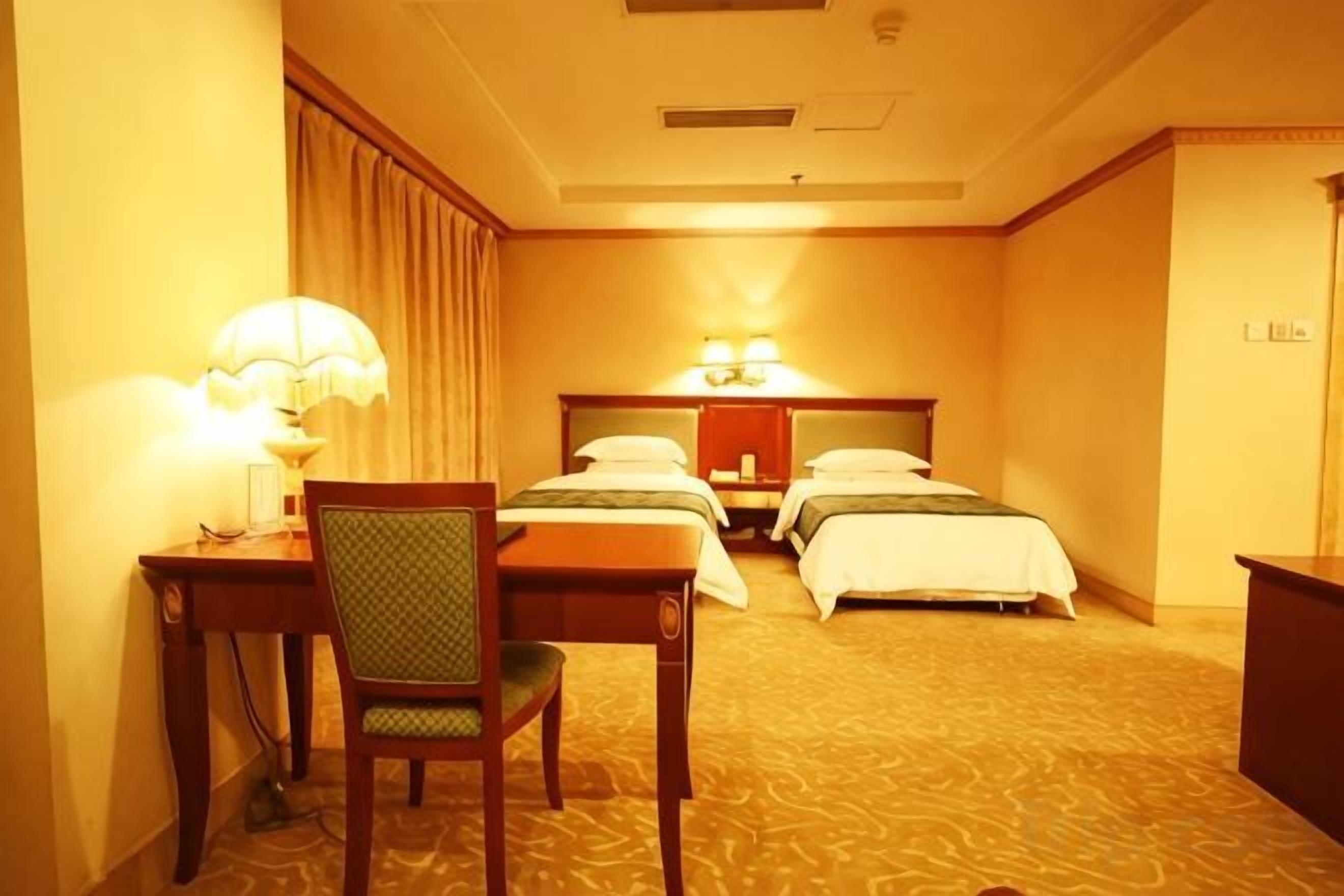 A hotel room with two beds, a desk with a chair, and a lamp.