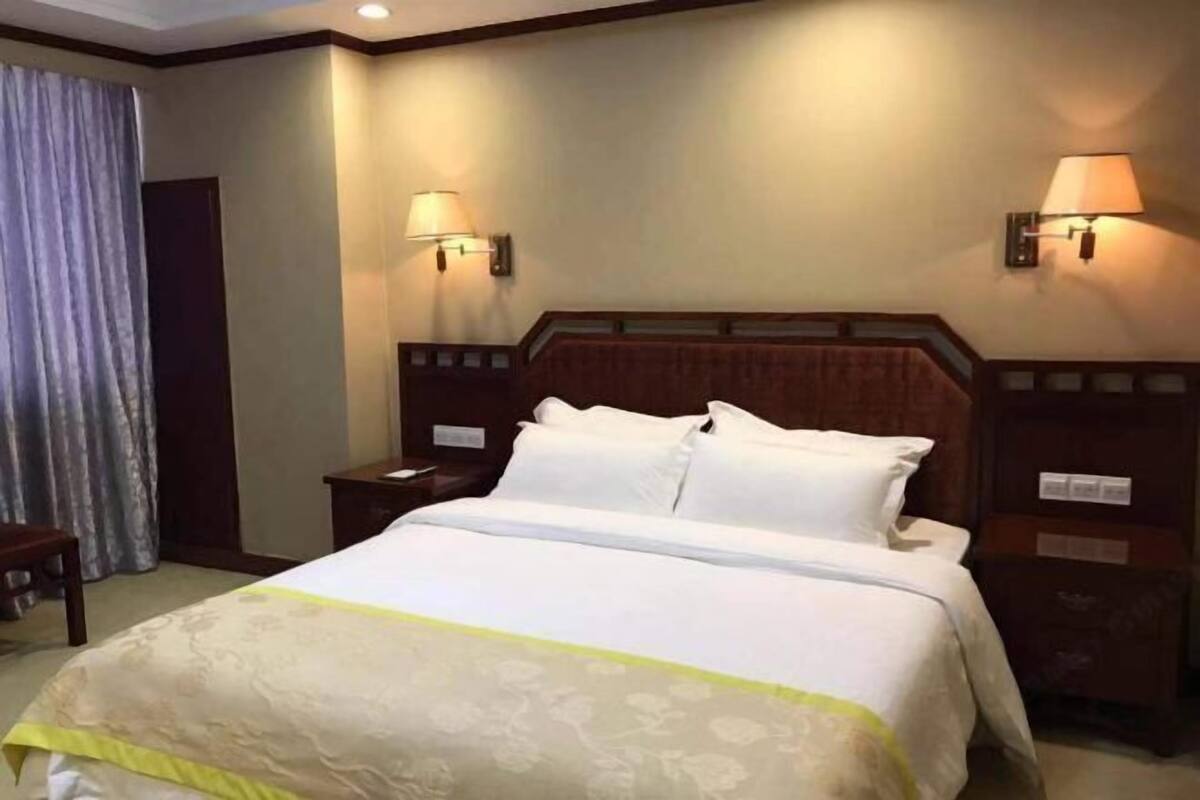 Een hotelkamer met een groot bed, twee bedlampen, een houten hoofdeinde en een nachtkastje.