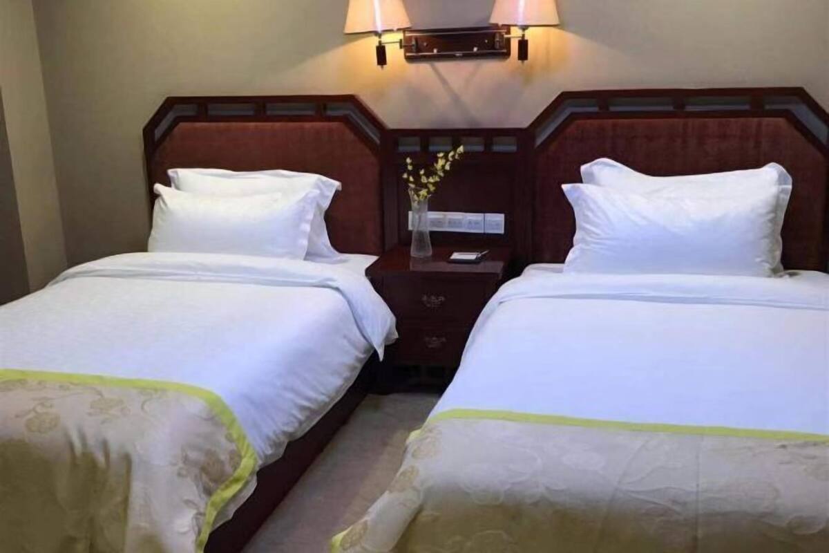 Een hotelkamer met twee bedden, een nachtkastje, een lamp en een vaas met bloemen.