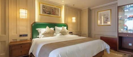 A hotel room with a large bed, bedside lamps, a wooden nightstand, a desk, and a framed picture on the wall.